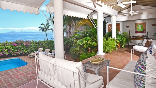 A covered outdoor area with a pool, lounge chairs, and a view of the ocean.