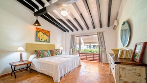 A bedroom with a bed, a nightstand, a lamp, a painting, a mirror, and a view of the outside.