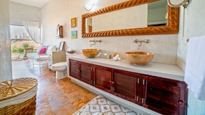 A bathroom with a large mirror, two bowls, a toilet, and a wicker chair.