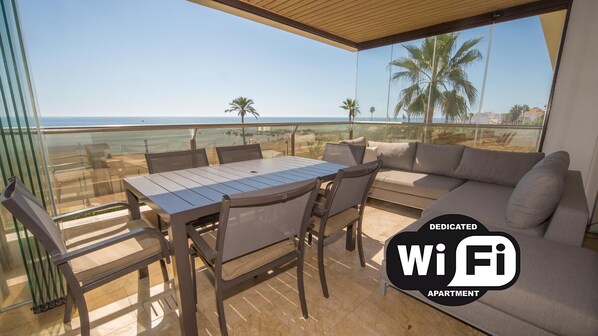 A balcony with a table and chairs, a sofa, and a view of the beach and ocean. - Marina del Castillo 319 (Manilva)