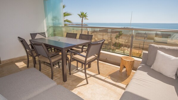Un balcón con mesa y sillas, un sofá y vista al mar.