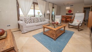 Uma sala de estar com um sofá, uma mesa de centro, uma poltrona e uma mesa de jantar.