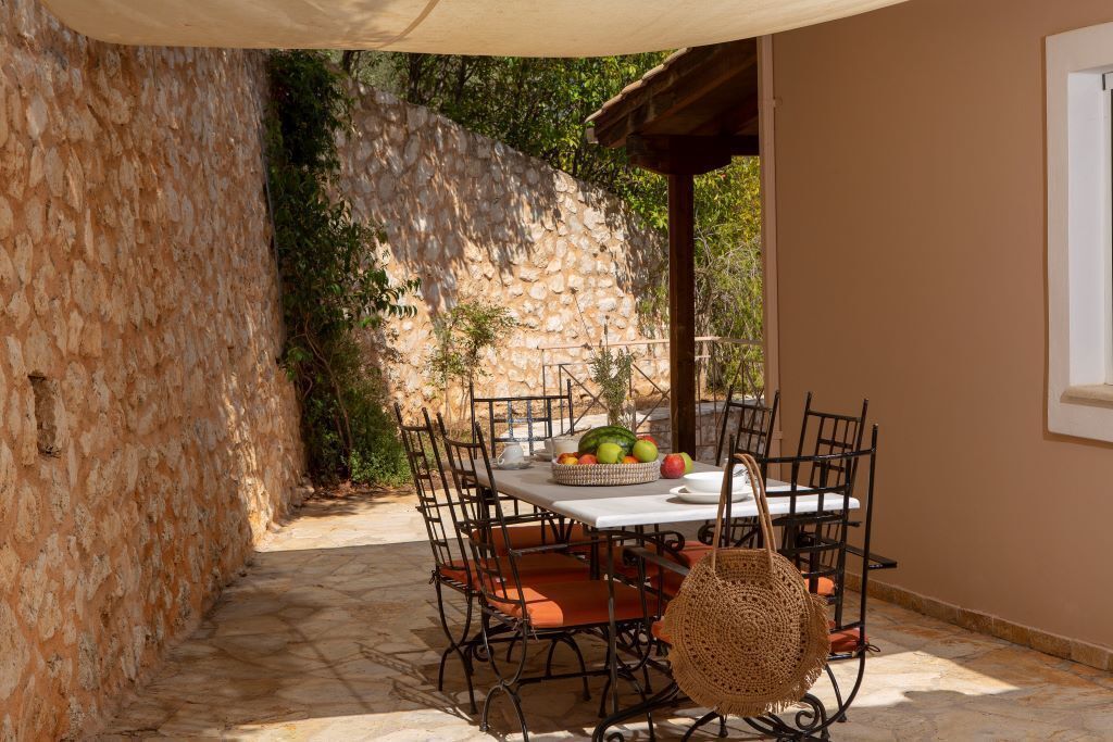 Een terras buiten met een stenen muur, een tafel met stoelen en een mand vol fruit.