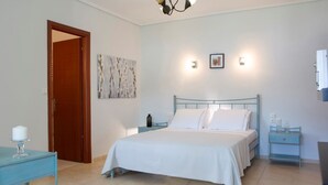 A bedroom with a bed, bedside tables, a nightstand, a door, and a wall-mounted light fixture. - Villa Eirini (Vasiliki Lefkada)