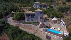 A hillside villa with a swimming pool, stone walls, and a paved driveway. - Villa Eirini (Vasiliki Lefkada)