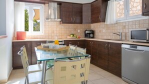 A modern kitchen with dark wooden cabinets, a glass dining table, and stainless steel appliances. - Villa Eirini (Vasiliki Lefkada)