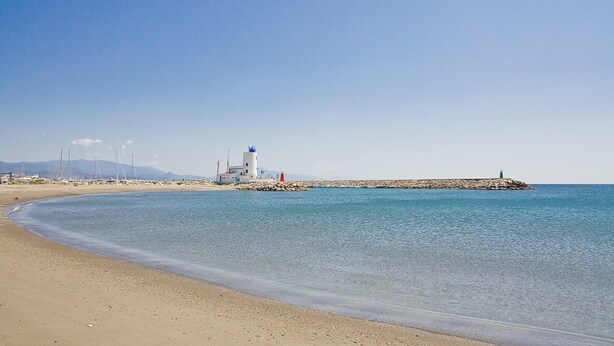 A coastal scene with a lighthouse, beach, and rocky breakwater. - Marina del Castillo 321 (Manilva)