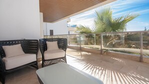A balcony with two wicker chairs and a table, overlooking a palm tree and a clear sky. - Marina del Castillo 321 (Manilva)