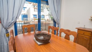 A dining area with a wooden table, chairs, and a wicker basket. - Mikonos Playa apto 19 (Manilva)