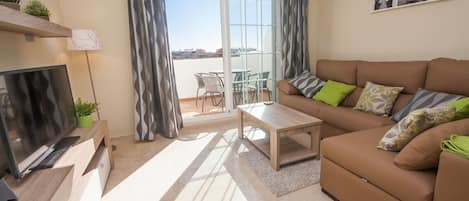 A modern living room with a flat-screen TV, a sofa with patterned cushions, a coffee table, and a sliding glass door leading to an outdoor area.