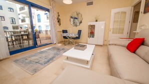 A living room with a sofa, coffee table, and a dining area with chairs and a table. - Mikonos Playa 14 (Manilva)