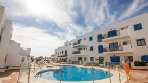 A swimming pool surrounded by white buildings with blue accents, clear skies, and a lifebuoy near the pool. - Mikonos Playa 14 (Manilva)