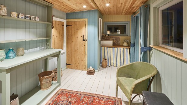 A cozy room with a wooden ceiling, a green chair, a small table, and a window with curtains. - Tilldene (New Romney)