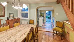 A dining area with a wooden table and chairs, a chandelier, and a view of the garden through an archway. - Tilldene (New Romney)