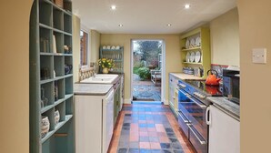 A kitchen with a tiled floor, a sink, and a stove. There is a door leading to a garden. - Tilldene (New Romney)