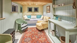 A cozy room with a bed, two chairs, a small table, and shelves with kitchenware. - Tilldene (New Romney)