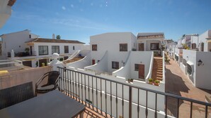 Et boligområde med hvide bygninger, en trappe og en balkon med bord og stole.