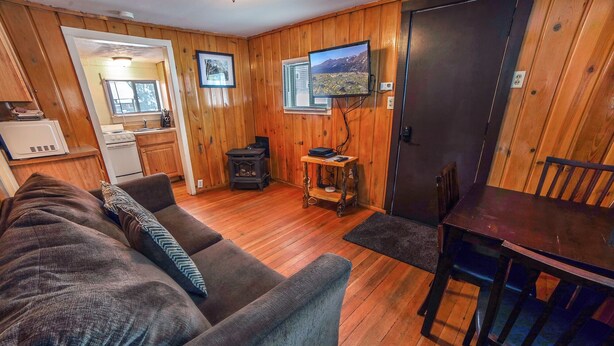 A cozy living room with a wooden floor, a sofa, a dining table, and a television mounted on the wall. - Cabin offers a rustic and cozy getaway (Estes Park)