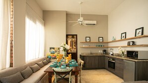 Een moderne woonkamer met een bank, een eettafel en stoelen. Er is een keukenhoek met een magnetron, broodrooster en kastjes.