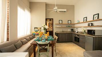A modern living room with a sofa, dining table, and chairs. There is a kitchen area with a microwave, toaster, and cabinets.