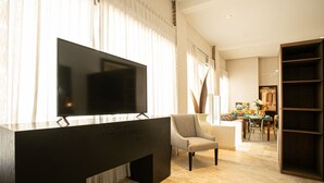 Een moderne woonkamer met een grote flatscreen televisie, een donkere houten dressoir, een grijze fauteuil en een eethoek met een tafel en stoelen.