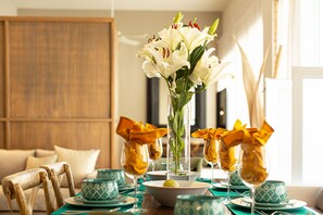 A dining table set with green patterned bowls, clear glassware, and a vase of white lilies.