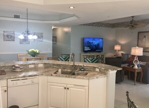 A modern kitchen with a built-in island, a dining area with chairs, a television, and a ceiling fan. - Naples Golf course Community Condo (Naples)