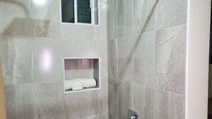 Zona de ducha con estante empotrado para toallas y una ventana encima.