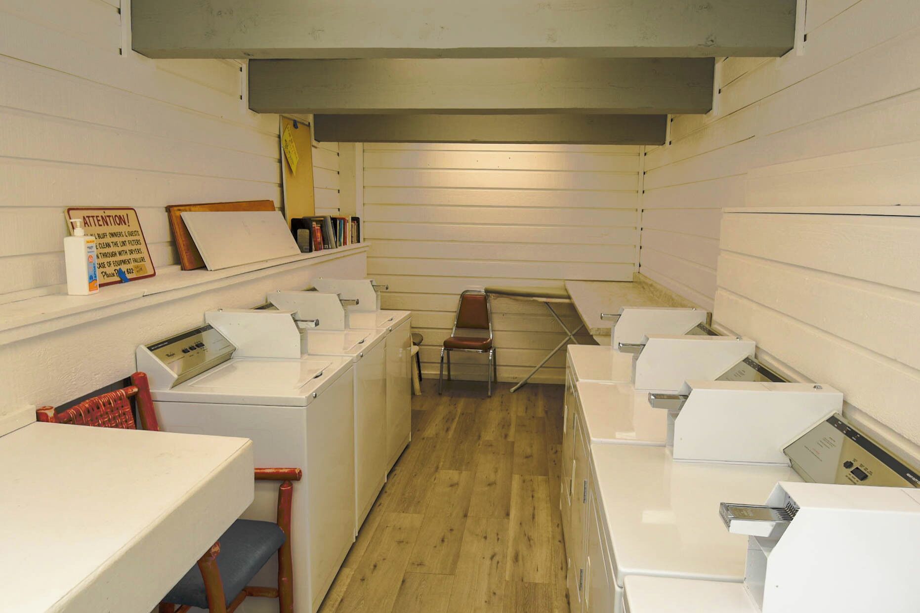 Une buanderie équipée de plusieurs machines à laver, d’une table à repasser et d’une chaise.
