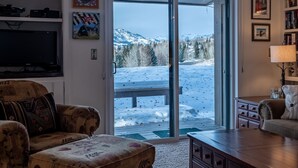 A living room with a large TV, a sofa, a coffee table, and a view of a snowy landscape through a glass door.