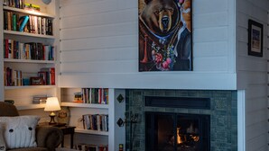 A cozy living room with a fireplace, bookshelves, and a bear-themed artwork.
