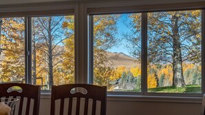 A dining area with a table and chairs, large windows with a view of autumn trees and a mountain.
