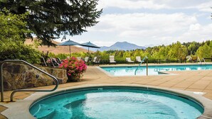 A pool area with two pools, lounge chairs, and a stone wall with a flower pot.