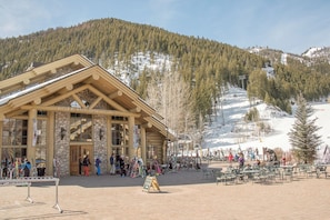 Un chalet à la façade en pierre, avec des poutres en bois, et une piste de ski en arrière-plan.