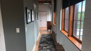Un pasillo con alfombra estampada, piso de madera y ventanas amplias con marcos de madera.