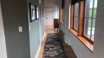 Un couloir avec un tapis à motifs, un plancher en bois et de grandes fenêtres avec des cadres en bois.