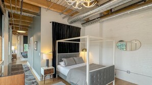 Un dormitorio moderno con cama con dosel, una mesita de noche pequeña, una lámpara y un espejo en la pared.