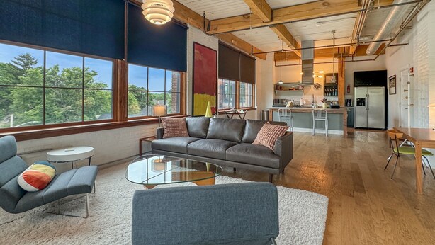 Un salón moderno con un sofá de cuero, una mesa de centro de vidrio y vistas a la cocina y el comedor.
