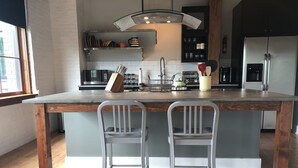 Una cocina moderna con una isla central, dos taburetes de bar y un refrigerador de acero inoxidable.