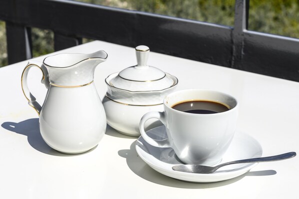 A white table with a white pitcher, a white teapot, and a white cup with a saucer and spoon. - Maria Apartments (Epidaurus)