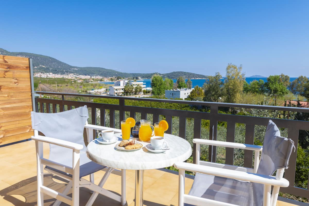 A terrace with a table set for breakfast, overlooking a scenic view of a coastal town and hills.