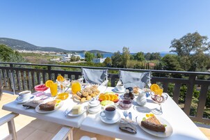 Una mesa de desayuno con diversas comidas y bebidas, con vistas a un paisaje pintoresco con colinas y una masa de agua.