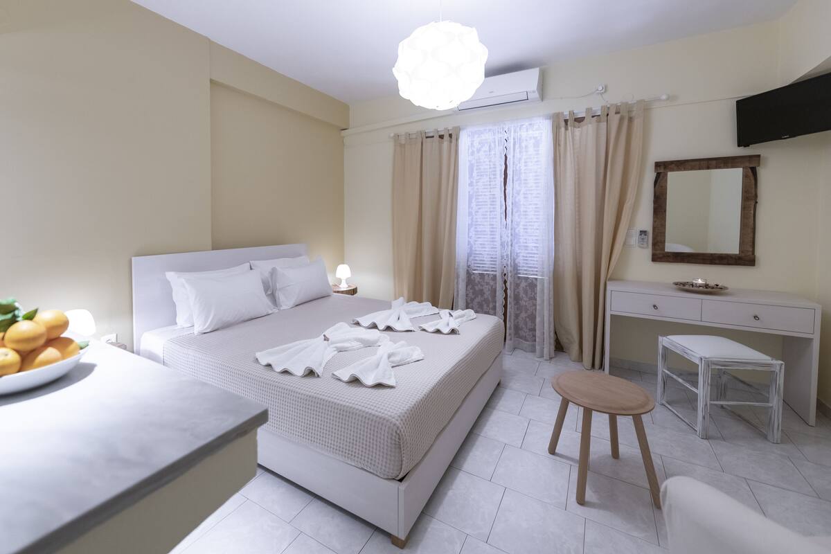 A modern hotel room with a bed, a desk, a chair, and a small table with fruit on it.