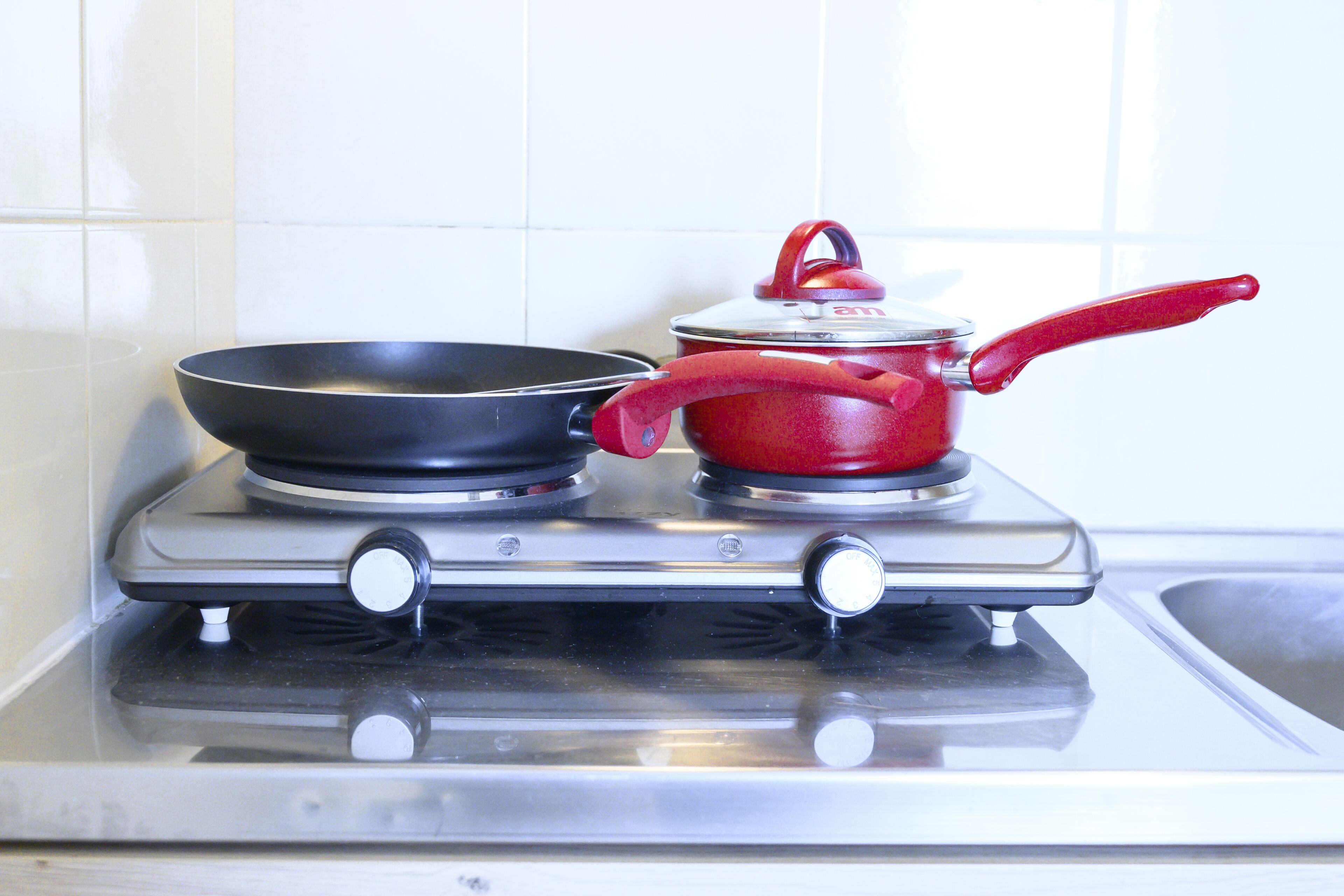 A kitchen with a gas stove, a frying pan, and a red pot.
