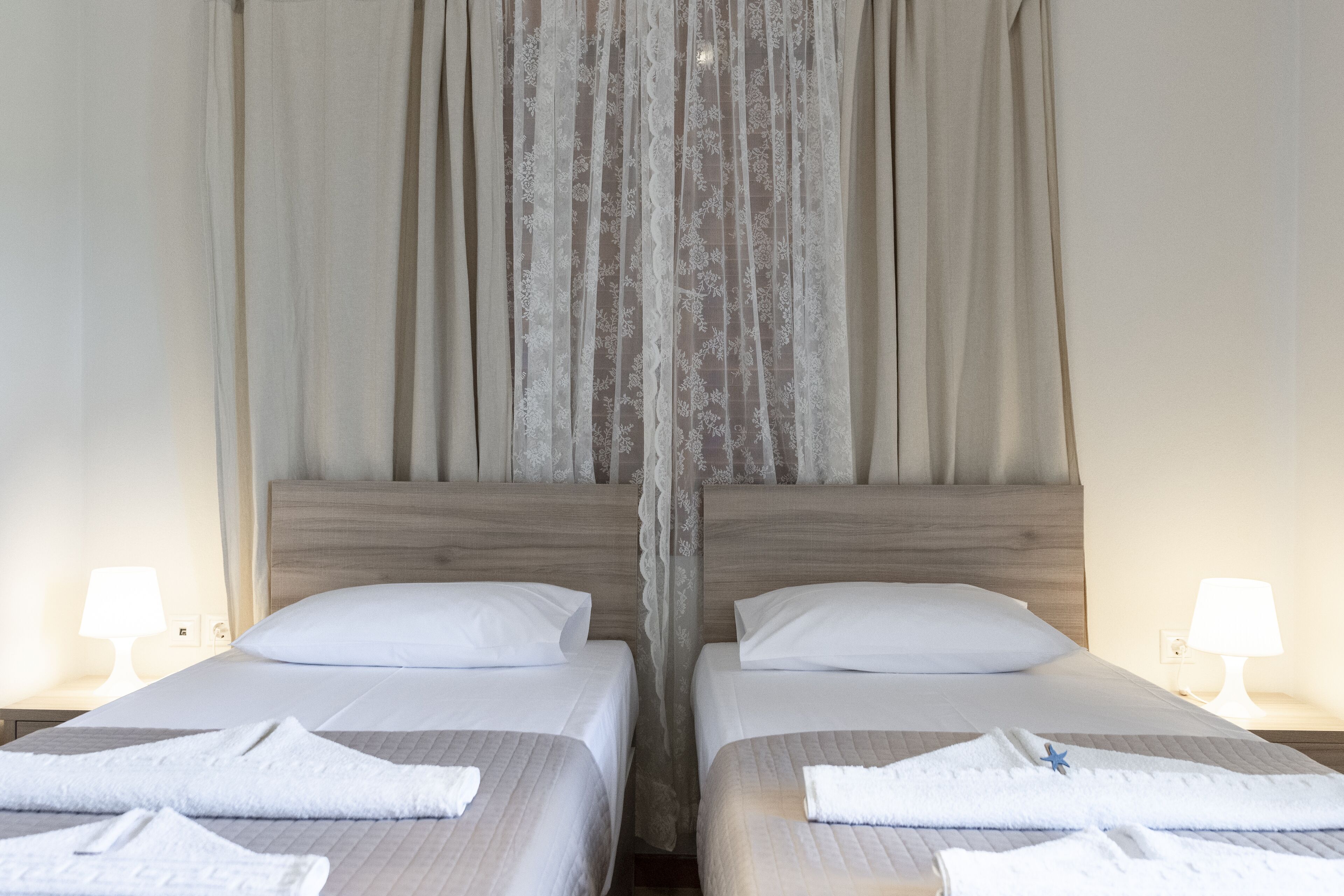 Habitación de hotel con dos camas, cada una con una almohada blanca y una toalla doblada con cuidado.