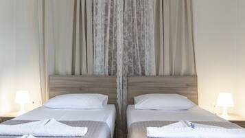 Habitación de hotel con dos camas, cada una con una almohada blanca y una toalla doblada con cuidado.