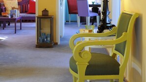 A room with a yellow wall, a green armchair, a red sofa, and a black lamp. - Chroma Design Hotel and Suites (Nafplio)