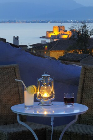 A table with a lantern, a drink, and a glass of water, overlooking a historic building by the water. - Chroma Design Hotel and Suites (Nafplio)