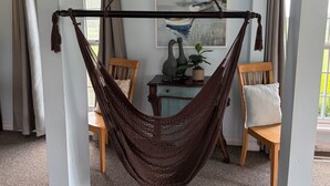 Eine Hängematze, die zwischen zwei Stühlen gespannt ist, in einem Raum mit einem Bild an der Wand und einem Fenster mit Vorhängen.