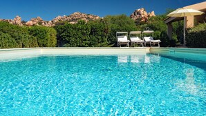 Una piscina azul cristalina con sillones de descanso y una pérgola.